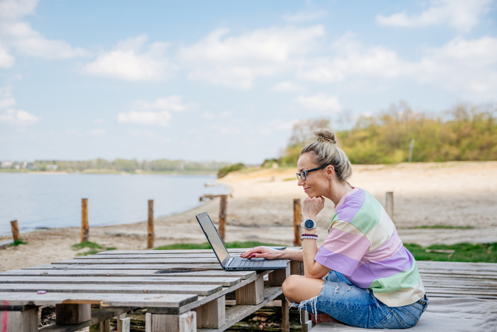 Télétravail: jeune femme travaillant sur son ordinateur au bord d'un lac